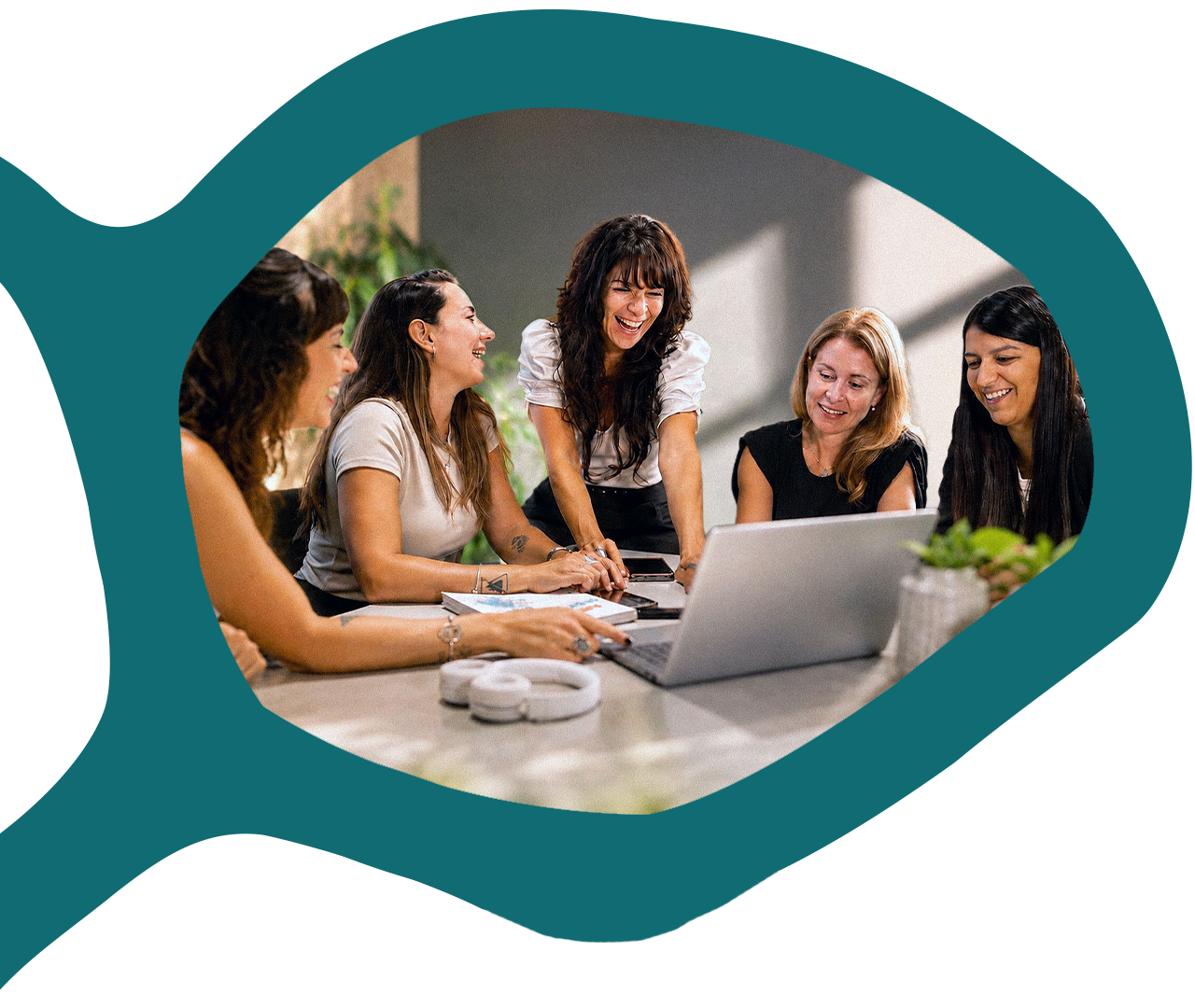 Cinco mujeres ríen alrededor de una notebook durante una reunión de trabajo.