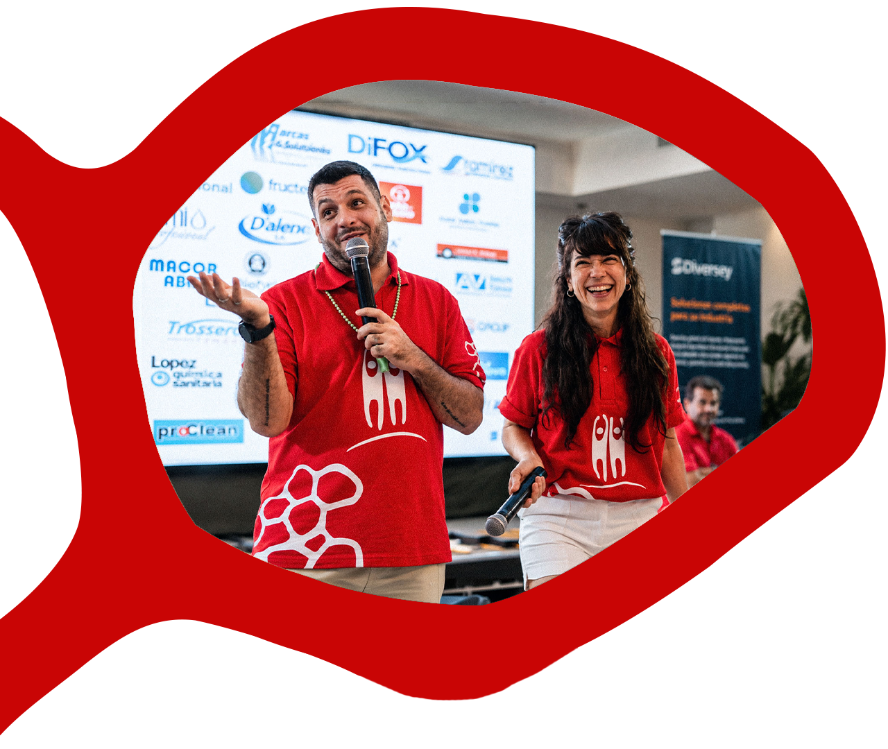 Dos facilitadores de Activos Humanos conducen un evento con micrófonos frente a una pantalla con logos de empresas.